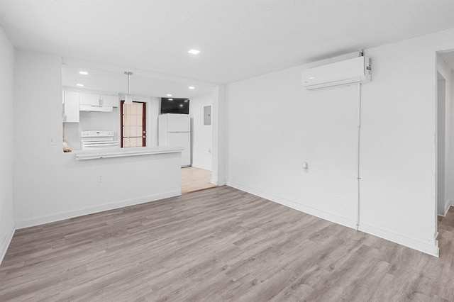 unfurnished living room with an AC wall unit, electric panel, and light hardwood / wood-style flooring