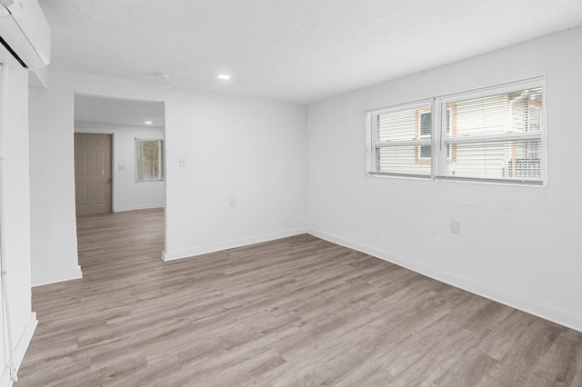 spare room with a textured ceiling, a wall mounted AC, and light hardwood / wood-style flooring