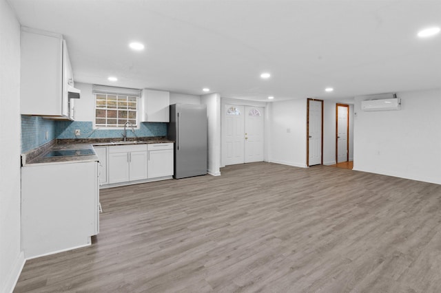 kitchen featuring a wall unit AC, stainless steel refrigerator, white cabinets, and light wood-type flooring