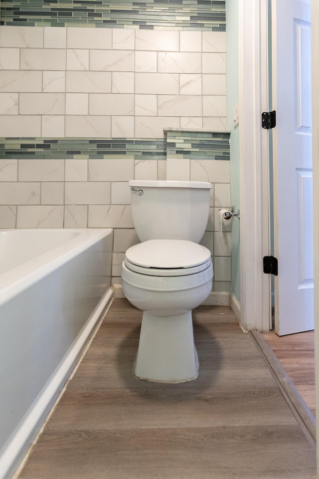 bathroom with toilet, hardwood / wood-style floors, tile walls, and a tub to relax in