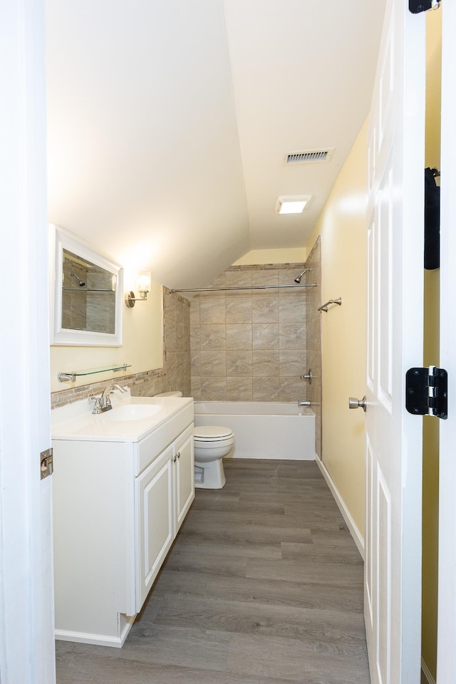 full bathroom with vaulted ceiling, tiled shower / bath, hardwood / wood-style flooring, vanity, and toilet