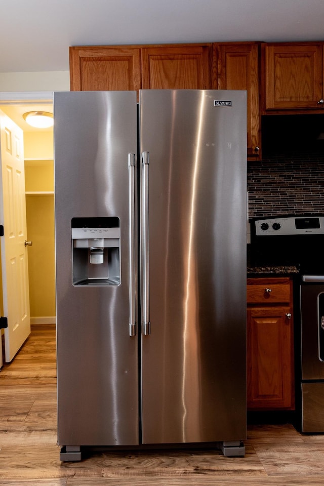 kitchen with tasteful backsplash, light wood-type flooring, dark stone counters, and appliances with stainless steel finishes