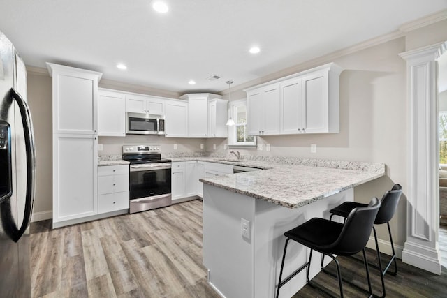 kitchen featuring kitchen peninsula, ornamental molding, stainless steel appliances, white cabinetry, and hanging light fixtures