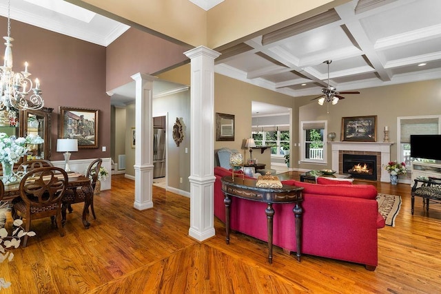 living room with beam ceiling, decorative columns, wood-type flooring, a tiled fireplace, and ornamental molding