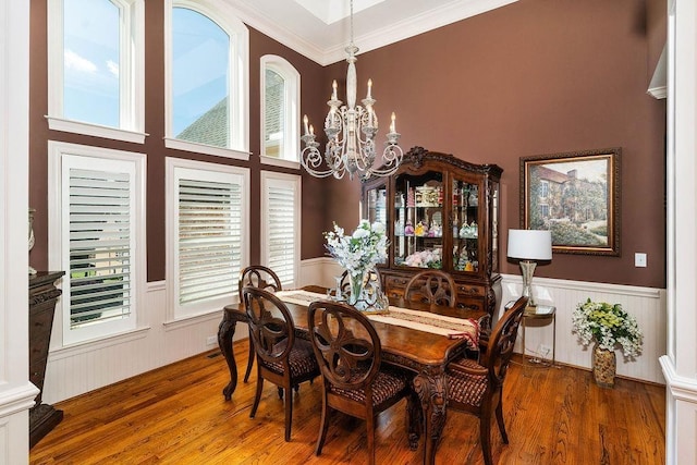 dining space featuring wood-type flooring, a towering ceiling, an inviting chandelier, and crown molding