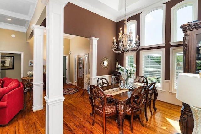 dining space with ornate columns, a towering ceiling, wood-type flooring, and a notable chandelier