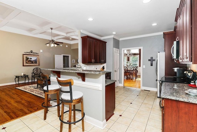 kitchen with a breakfast bar, light wood-type flooring, dark stone counters, and coffered ceiling