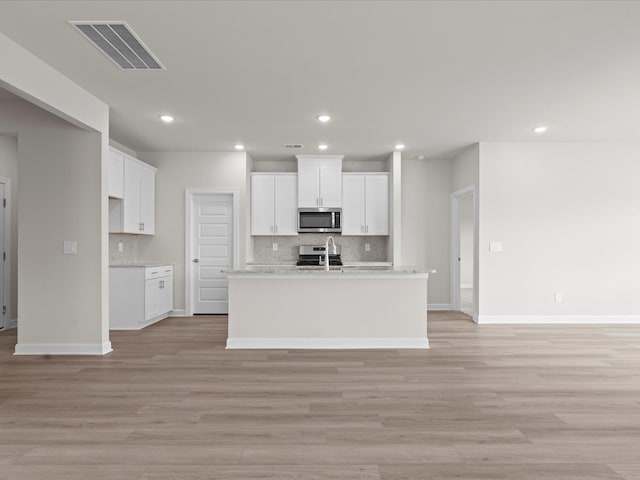 kitchen with white cabinetry, an island with sink, and light wood-type flooring