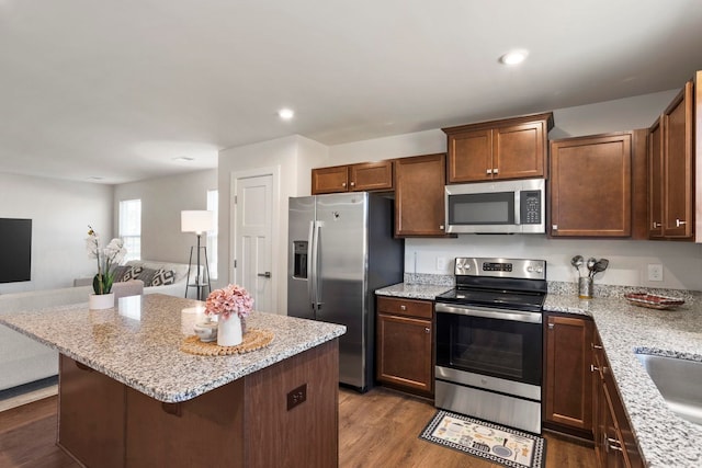 kitchen with appliances with stainless steel finishes, light stone counters, dark wood-type flooring, a kitchen island, and a breakfast bar area