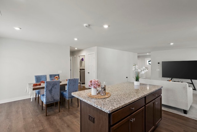 kitchen with a center island, dark hardwood / wood-style flooring, dark brown cabinetry, and light stone counters