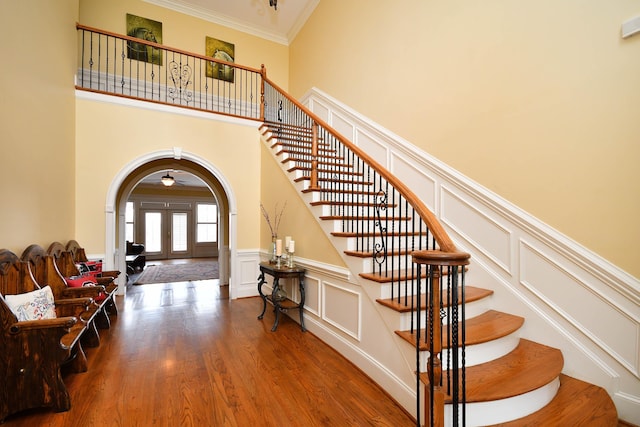 stairway with french doors, hardwood / wood-style flooring, crown molding, and a high ceiling