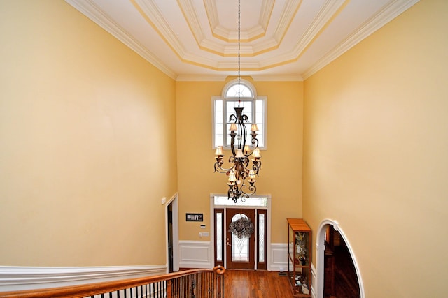 foyer entrance with a raised ceiling, hardwood / wood-style flooring, a notable chandelier, and ornamental molding