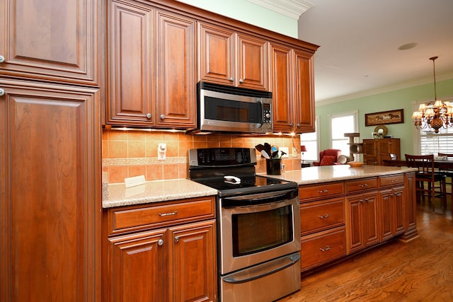 kitchen featuring a notable chandelier, ornamental molding, stainless steel appliances, and a wealth of natural light