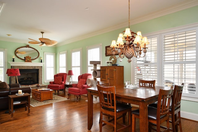 dining room featuring hardwood / wood-style flooring, ceiling fan with notable chandelier, a healthy amount of sunlight, and a brick fireplace