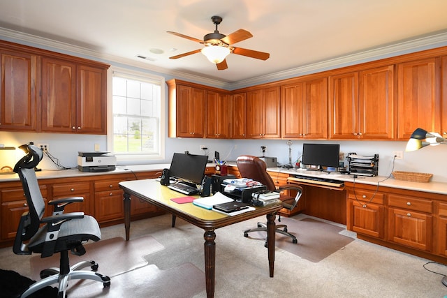 carpeted office with built in desk, ceiling fan, and crown molding