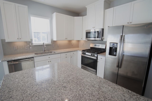 kitchen featuring white cabinets, sink, decorative backsplash, light stone countertops, and appliances with stainless steel finishes