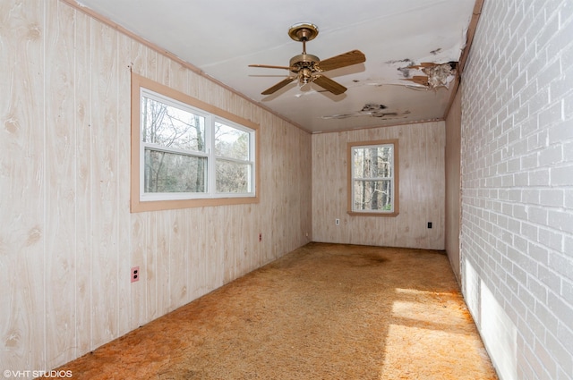 empty room featuring carpet, ceiling fan, a healthy amount of sunlight, and wooden walls