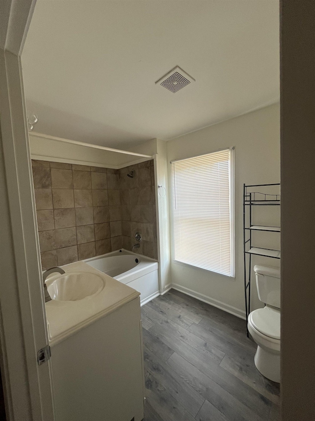 full bathroom featuring vanity, hardwood / wood-style floors, tiled shower / bath combo, and toilet