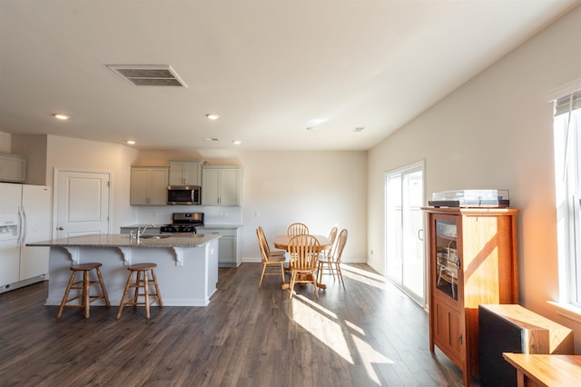 kitchen with a sink, visible vents, appliances with stainless steel finishes, light stone countertops, and dark wood finished floors