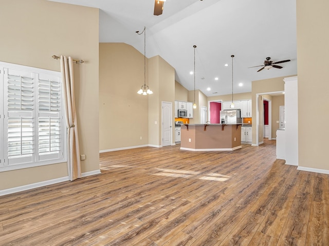 unfurnished living room featuring wood-type flooring, ceiling fan with notable chandelier, and lofted ceiling