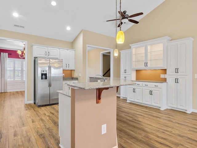 kitchen featuring stainless steel fridge with ice dispenser, ceiling fan, light stone counters, white cabinetry, and a breakfast bar area