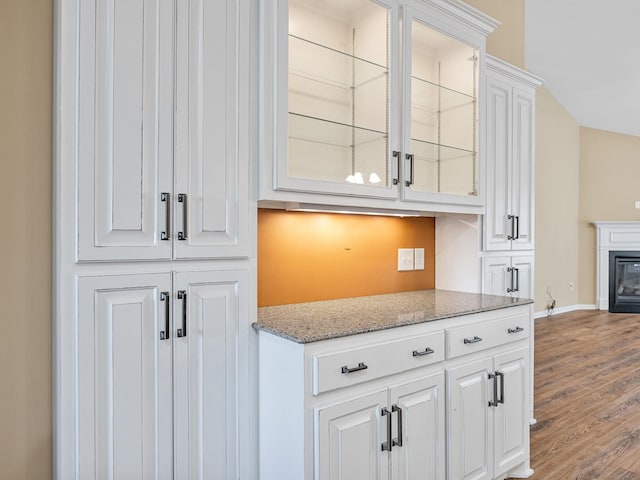 bar with white cabinetry, light stone counters, and wood-type flooring