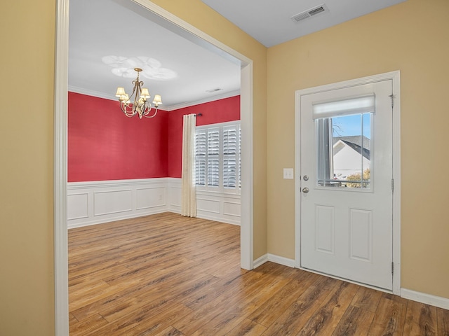 entryway with ornamental molding, a notable chandelier, and hardwood / wood-style flooring