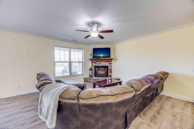 living room with light hardwood / wood-style flooring, ceiling fan, ornamental molding, and a stone fireplace