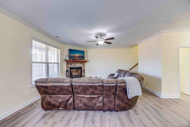 living room with a stone fireplace, ceiling fan, light hardwood / wood-style flooring, and ornamental molding