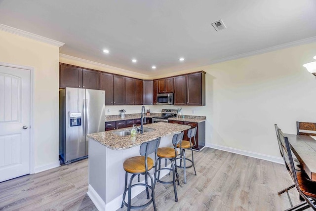 kitchen with light stone countertops, appliances with stainless steel finishes, ornamental molding, a breakfast bar, and sink