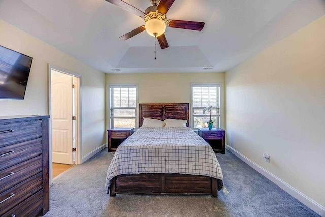 bedroom with multiple windows, light carpet, a raised ceiling, and ceiling fan