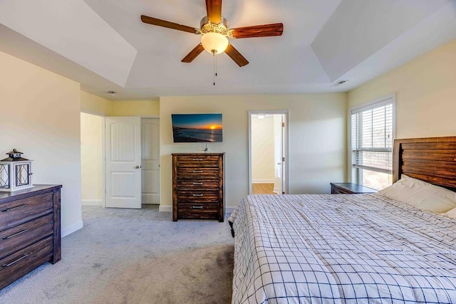 carpeted bedroom with a raised ceiling, connected bathroom, and ceiling fan