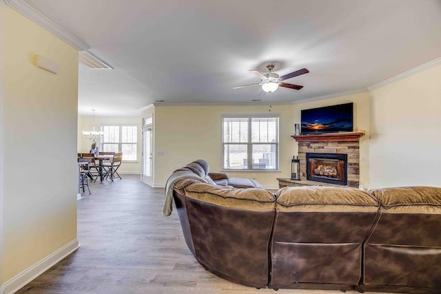 living room with wood-type flooring, ceiling fan with notable chandelier, a stone fireplace, and crown molding