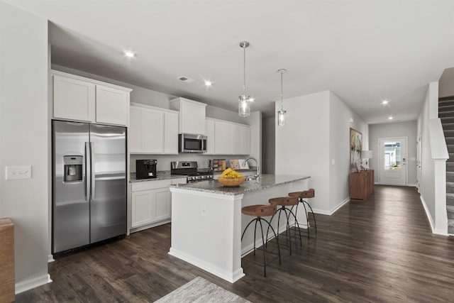 kitchen with stone counters, stainless steel appliances, white cabinetry, and a kitchen island with sink