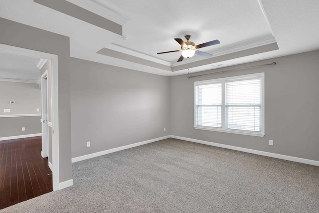 unfurnished room with a raised ceiling, ceiling fan, dark colored carpet, and ornamental molding