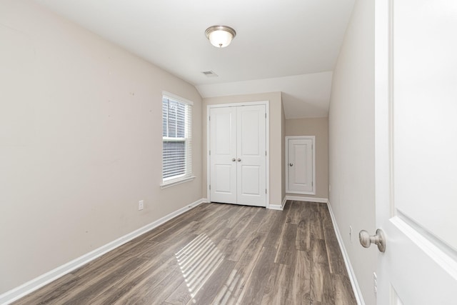 unfurnished bedroom featuring a closet, dark wood-type flooring, and lofted ceiling