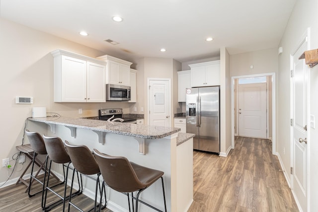 kitchen featuring kitchen peninsula, light hardwood / wood-style flooring, appliances with stainless steel finishes, white cabinetry, and a breakfast bar area