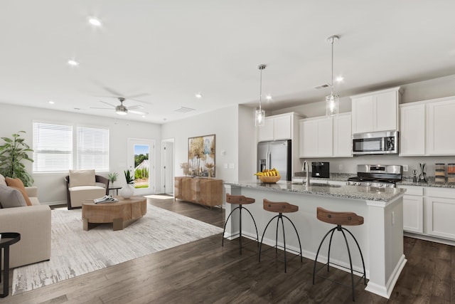 kitchen featuring a center island with sink, white cabinets, stainless steel appliances, and hanging light fixtures