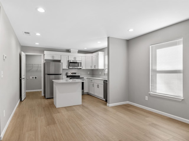 kitchen featuring appliances with stainless steel finishes, light wood-type flooring, sink, a center island, and white cabinetry