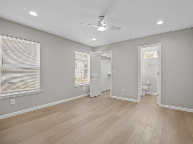 unfurnished bedroom with connected bathroom, a spacious closet, ceiling fan, a closet, and light wood-type flooring