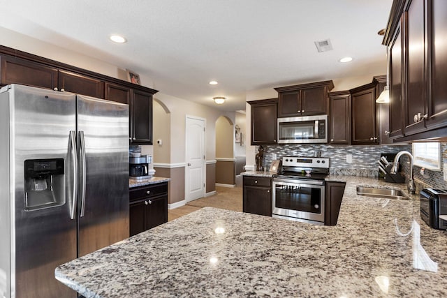 kitchen featuring dark brown cabinetry, light stone countertops, sink, stainless steel appliances, and decorative backsplash