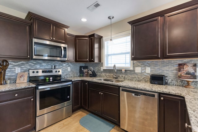 kitchen featuring light stone countertops, sink, hanging light fixtures, appliances with stainless steel finishes, and light wood-type flooring