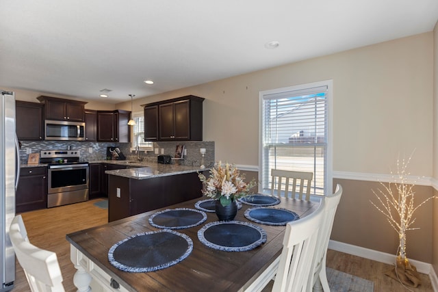 kitchen featuring light stone countertops, tasteful backsplash, pendant lighting, appliances with stainless steel finishes, and light wood-type flooring