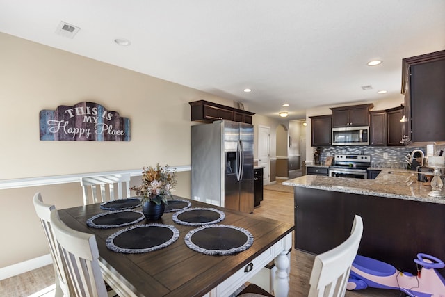 kitchen with kitchen peninsula, appliances with stainless steel finishes, tasteful backsplash, sink, and light hardwood / wood-style floors