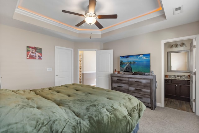 carpeted bedroom with ceiling fan, ornamental molding, connected bathroom, and a tray ceiling