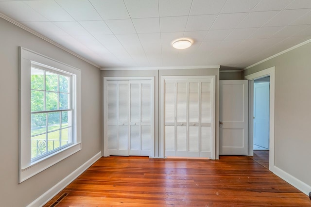 unfurnished bedroom featuring multiple closets, hardwood / wood-style floors, and ornamental molding