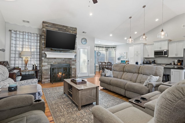 living room with a fireplace, light wood-type flooring, vaulted ceiling, and ceiling fan