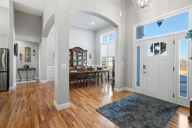 foyer entrance featuring an inviting chandelier, wood-type flooring, a high ceiling, and ornamental molding