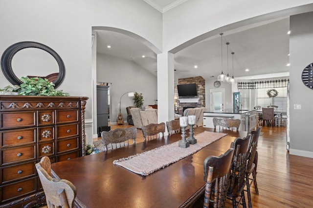 dining space with wood-type flooring, vaulted ceiling, a stone fireplace, and crown molding