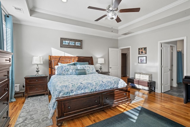 bedroom featuring ceiling fan, light hardwood / wood-style floors, ornamental molding, and a tray ceiling